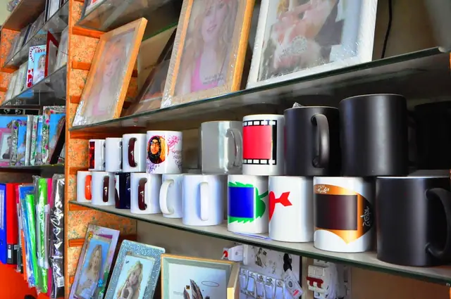 Printed mugs lined up on a shelf with photo frames below